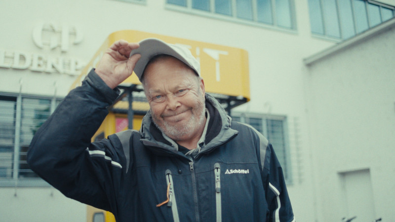Ein Farbfoto von Markus, einem älteren Herren, er steht vor der ZEITKAPSEL und zieht seine Kappe.