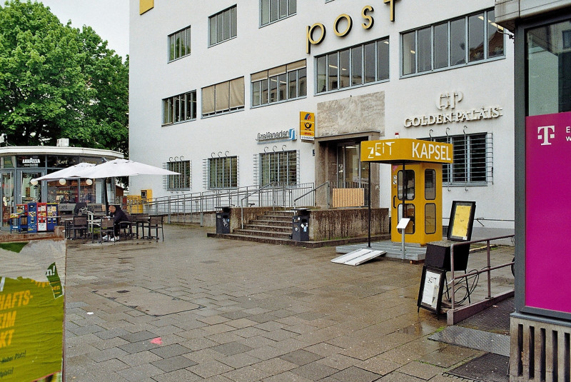Ein analoges Farbfoto von der ZEITKAPSEL (gelbe Telefonzelle mit Dachkonstruktion) vor der Postfiliale