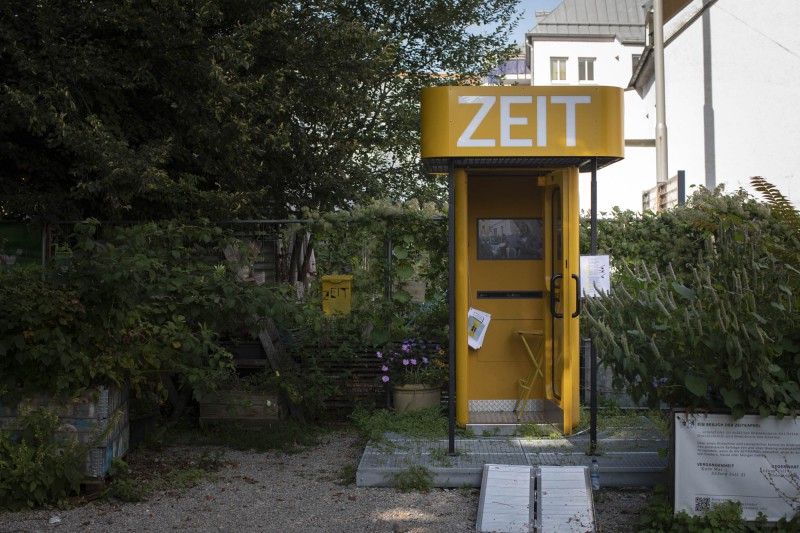 Ein Foto von der ZEITKAPSEL auf dem Giesinger Grünspitz, eine gelbe Telefonzelle mit einer Dachkonstruktion auf der 