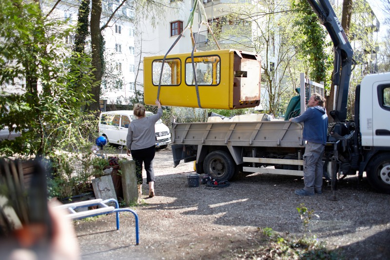 Die Telefonzelle wird mit einem Kranwagen transportiert. Zwei Helfer sind zu sehen.